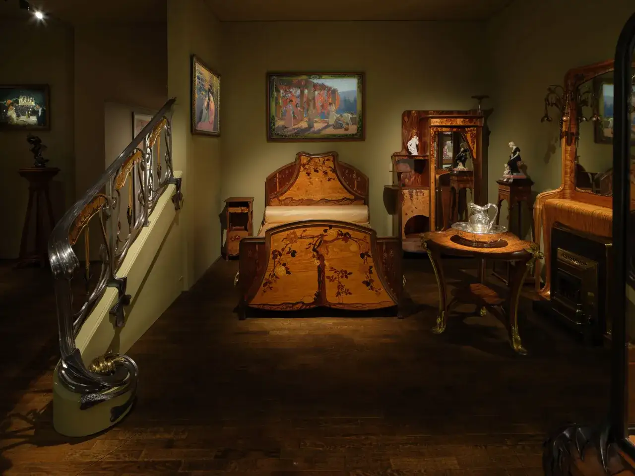 Chambre d'h&ocirc;tel meubl&eacute;e dans le style Art Nouveau, avec un lit orn&eacute; de marqueterie florale, une armoire sculpt&eacute;e et un escalier aux courbes organiques.