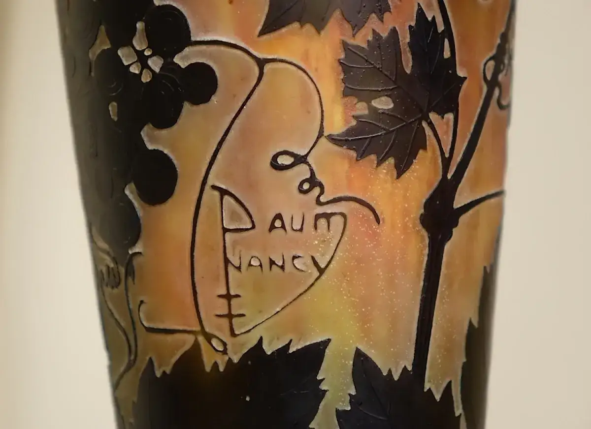 Gros plan sur un vase Daum Nancy, avec des grappes de raisin et des feuilles stylisées. L'estimation de ce vase Daum est une affaire d'expert.