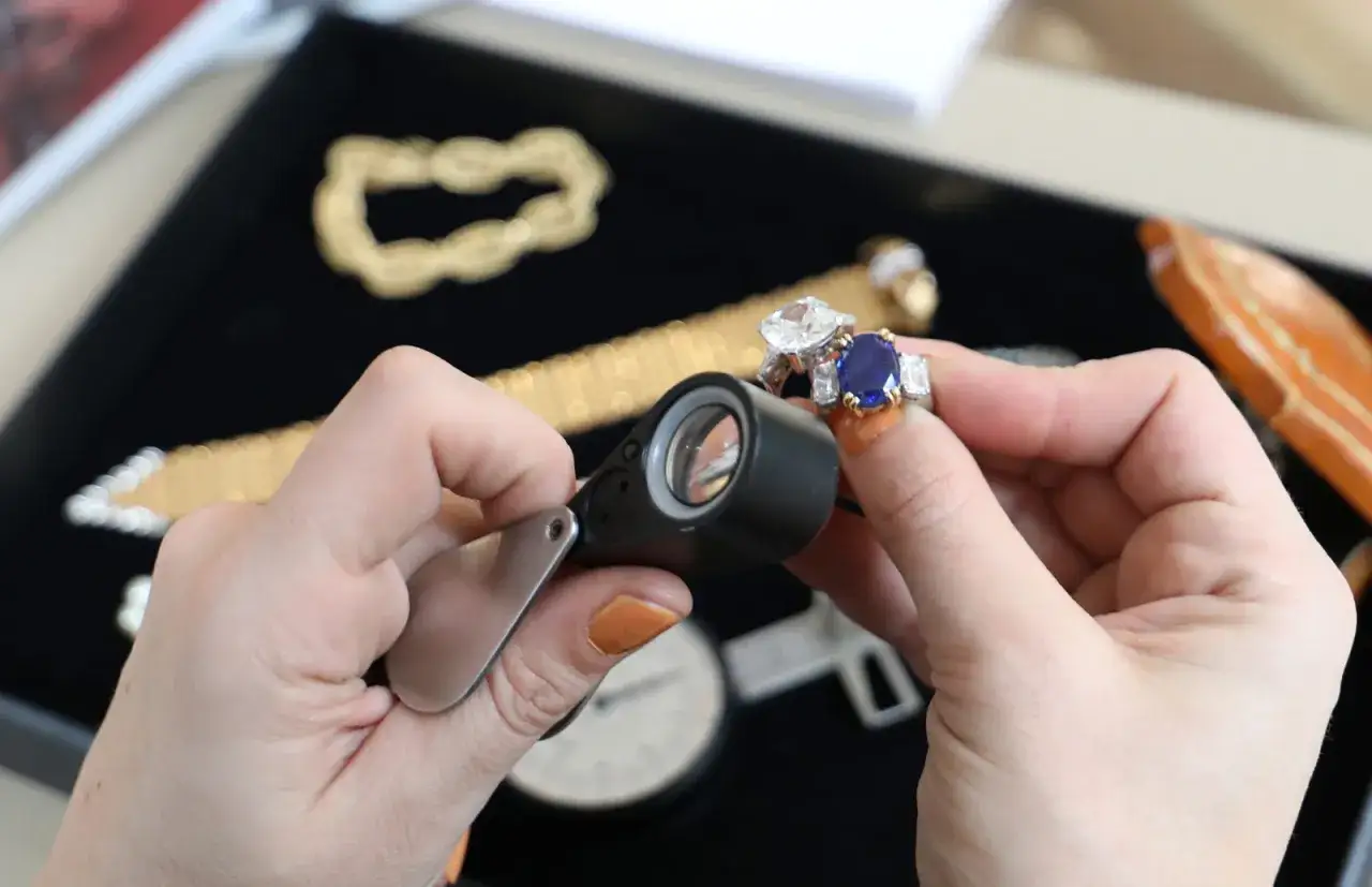 Maintenant, où faire expertiser des bijoux gratuitement ? Une loupe examine une bague saphir et diamant.