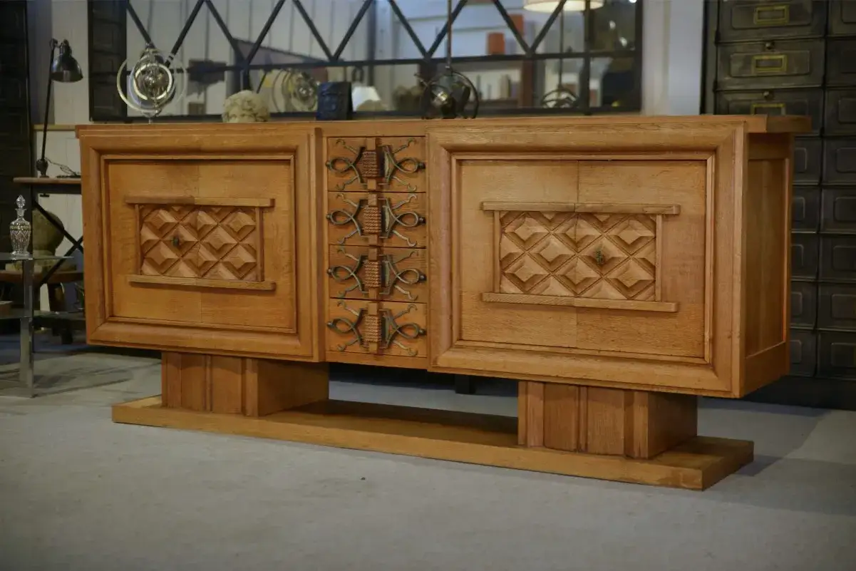 Buffet en ch&ecirc;ne massif, style Art D&eacute;co, sign&eacute; Charles Dudouyt. Ses portes sculpt&eacute;es et ses poign&eacute;es en fer forg&eacute; t&eacute;moignent d'un savoir-faire exceptionnel.