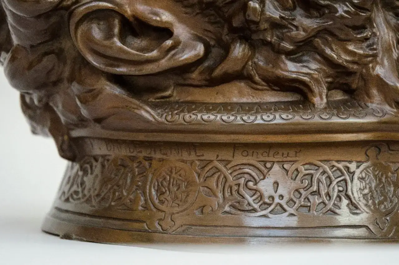 Détail d'une sculpture en bronze, creux ou plein, ornée de motifs complexes et d'une inscription gravée.