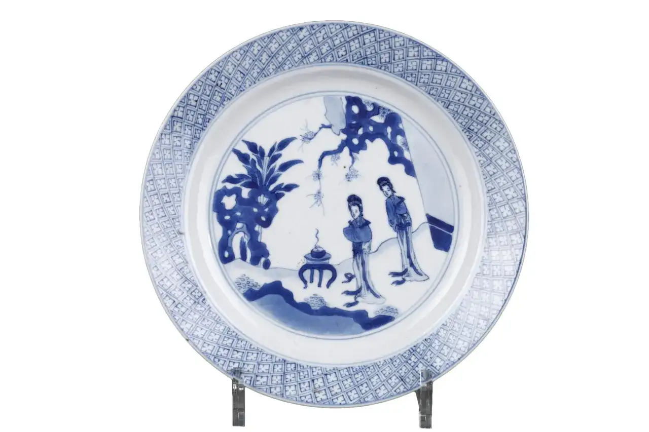Assiette chinoise ancienne signature, décorée de deux femmes dans un paysage stylisé, bordure ornée de motifs géométriques bleus.