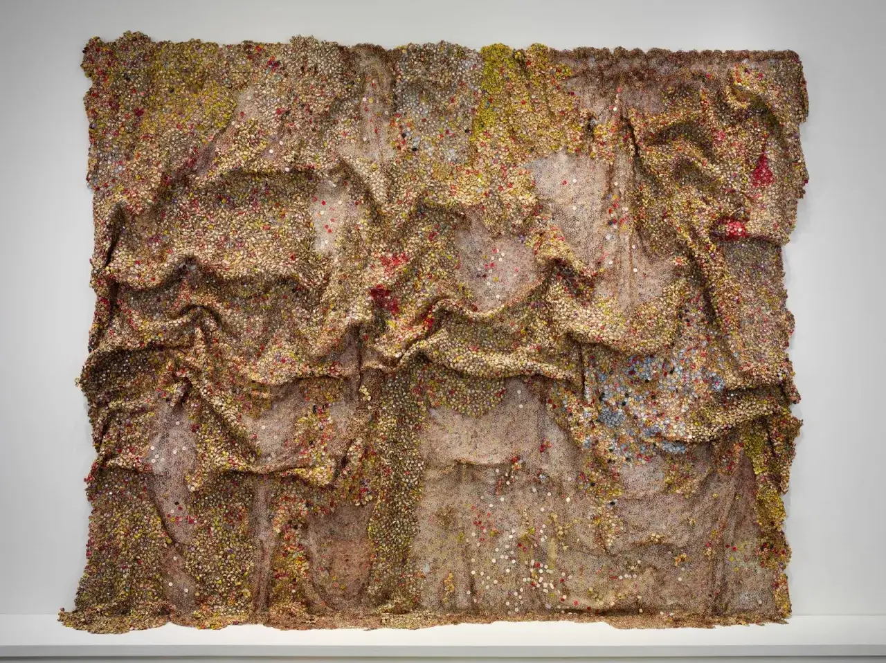 Œuvre d'El Anatsui, une tapisserie texturée de bouchons de bouteilles en aluminium, aux reflets dorés et cuivrés, évoquant des vagues ou des plis de tissu.