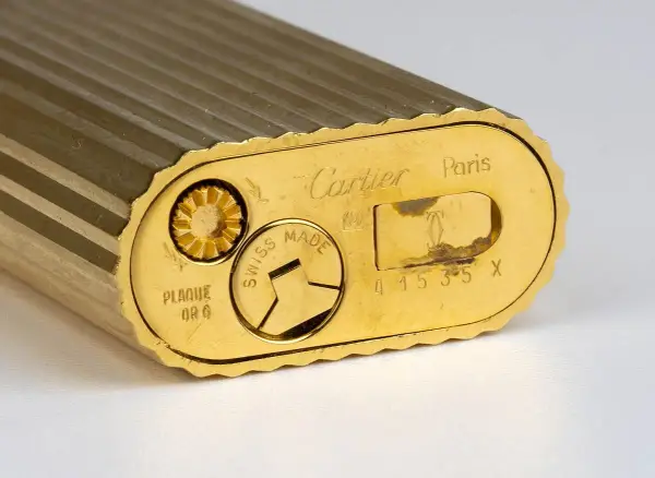 Gros plan sur le fond d'un briquet Cartier plaqué or, gravé "Swiss Made" et un numéro de série. Une pièce de collection pour une estimation.